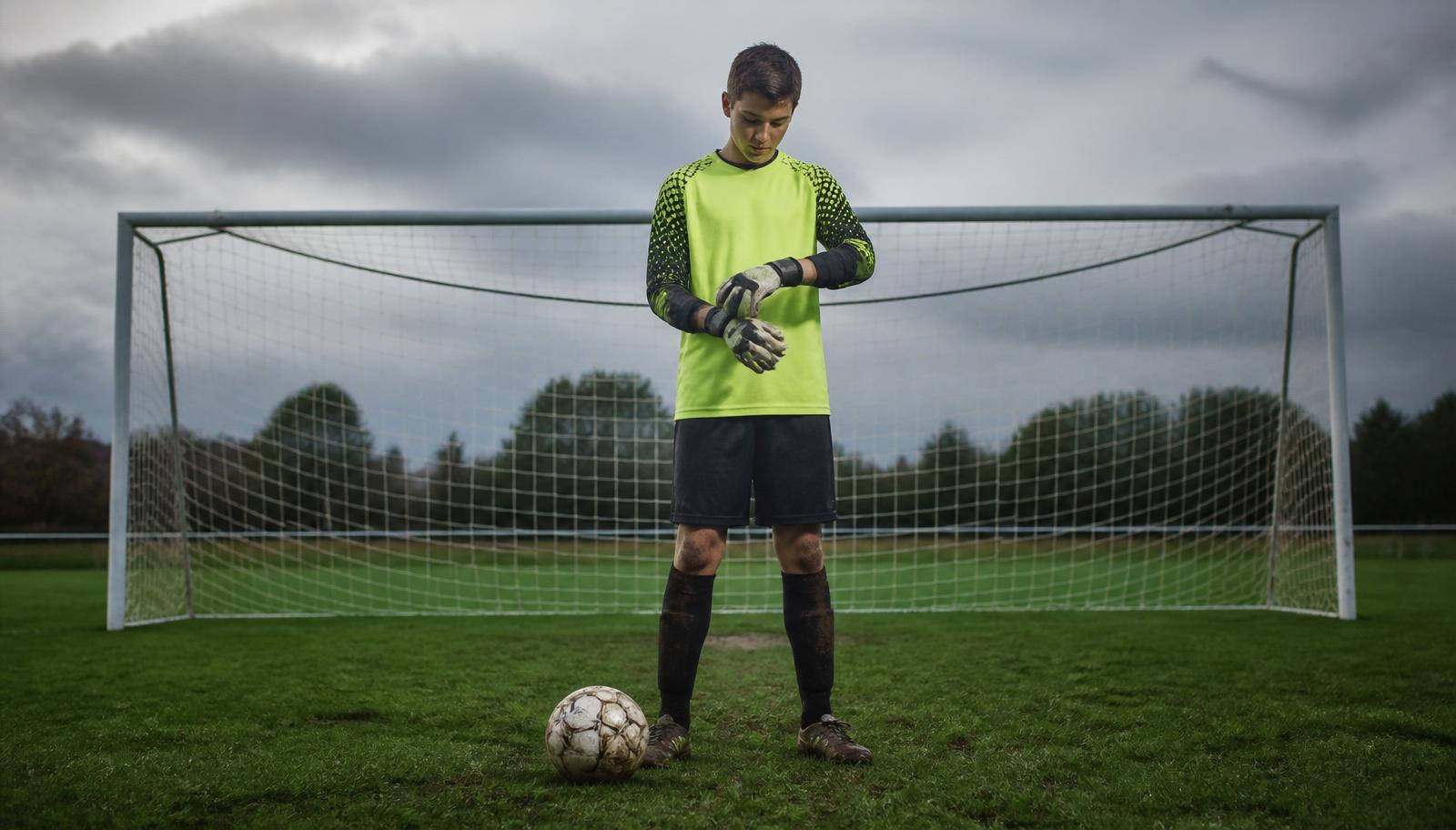 Young goalkeeper fastening gloves in front of a soccer goal on an overcast field
