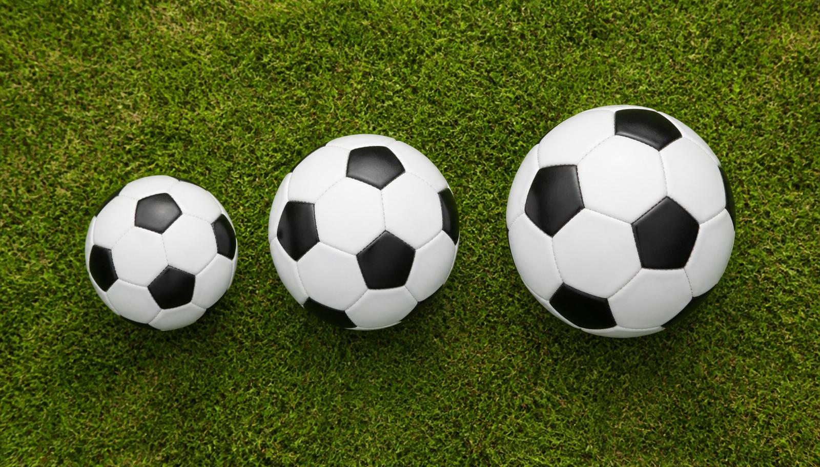 Youth soccer balls sizes 3, 4, and 5 lined up on green grass